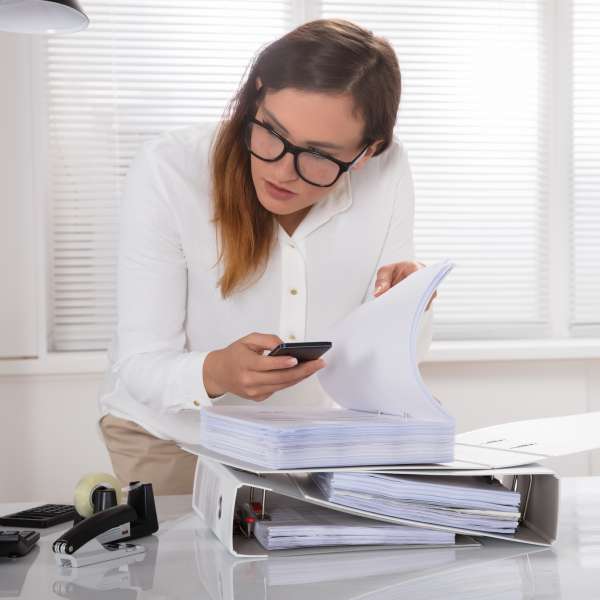 A real estate agent with documents on a folder and phone in hand