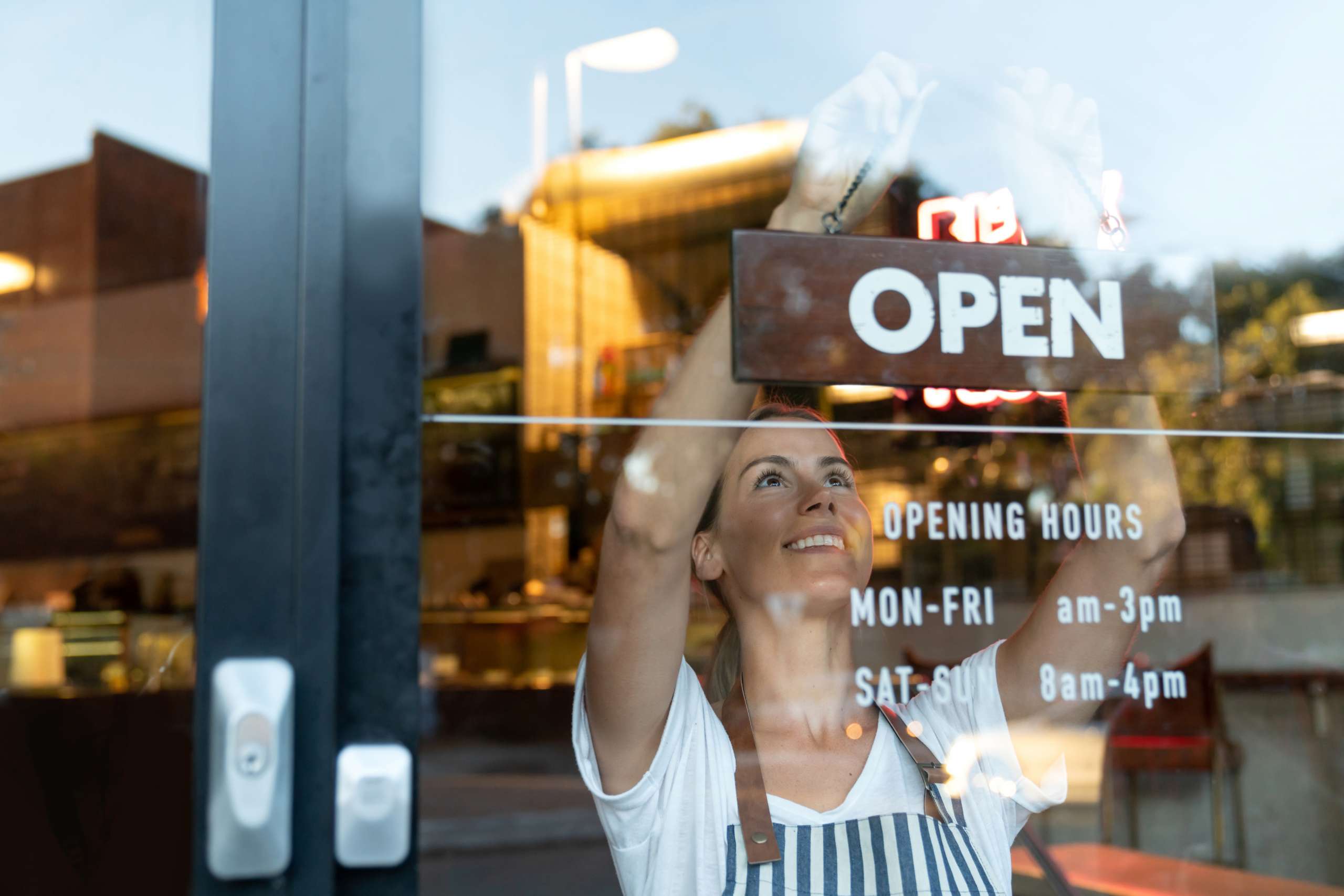 Happy business owner hanging an open sign at a cafe