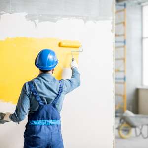 A painter paints yellow paint on indoor wall