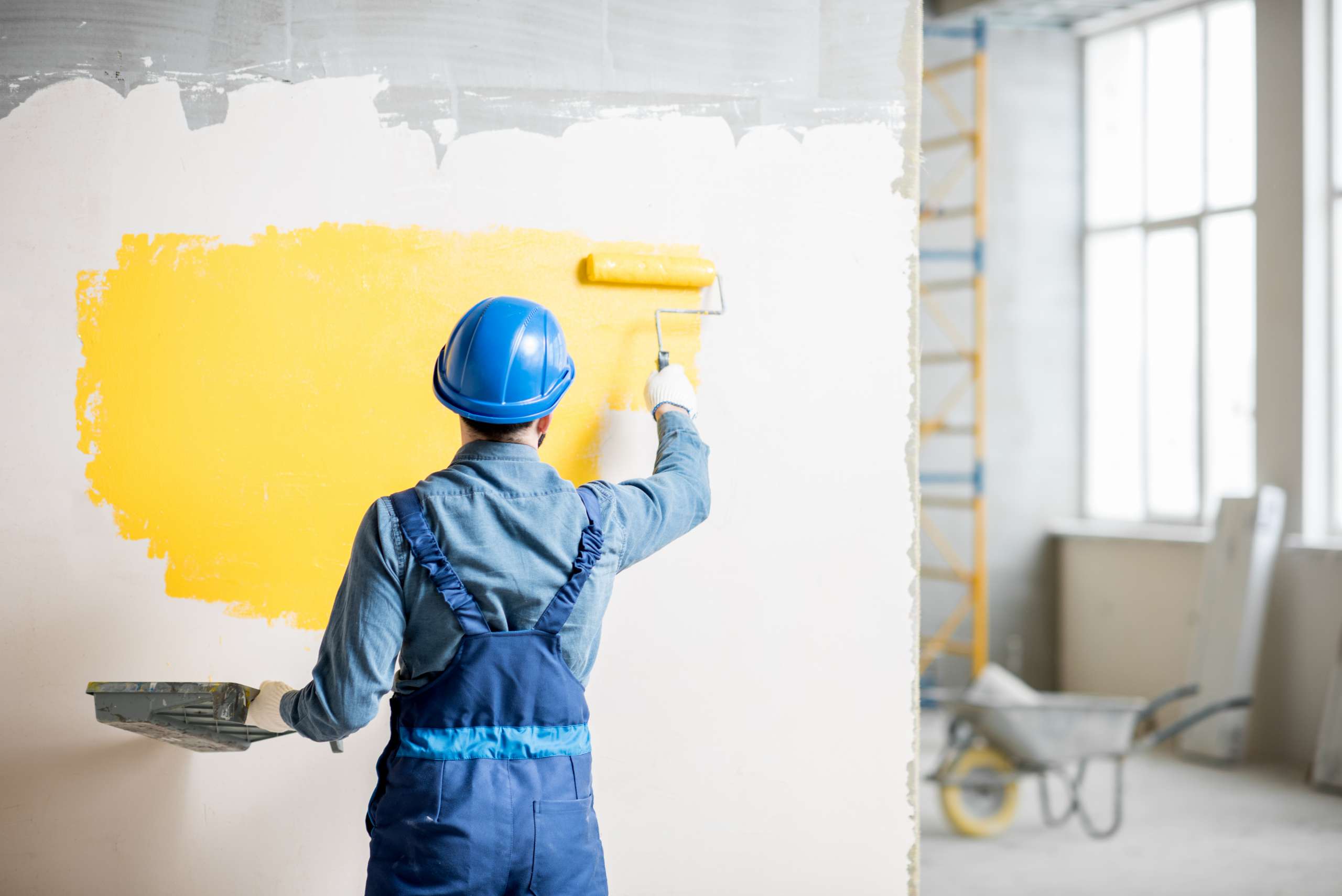 A painter paints yellow paint on indoor wall