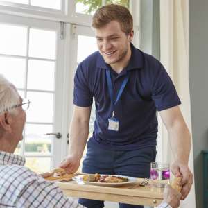 Care worker serving dinner to a senior man at home