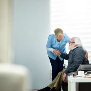 A nurse helps a senior man et up from couch