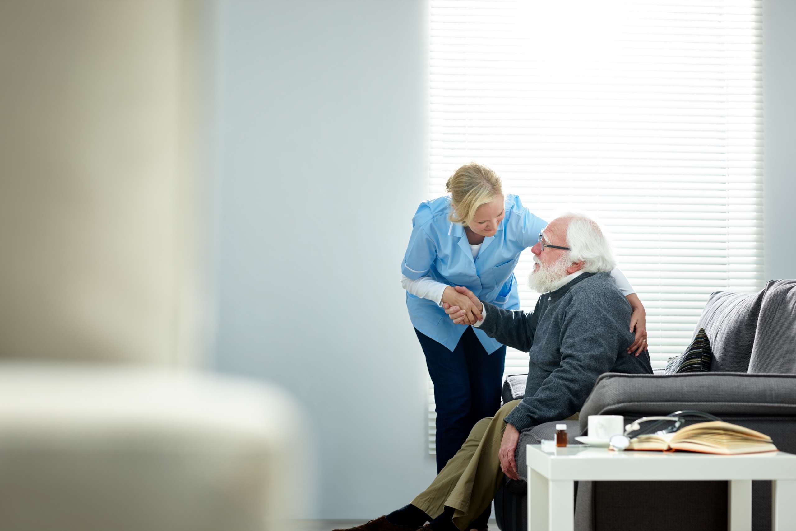 A nurse helps a senior man et up from couch