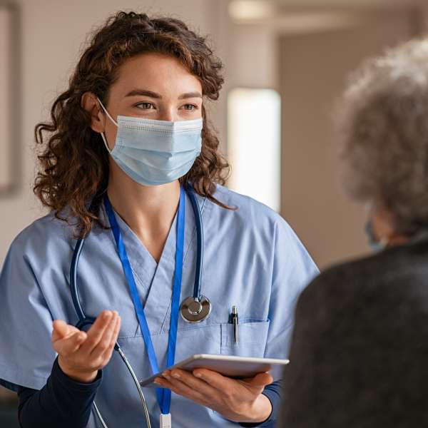 A nurse visits senior woman with surgical mask