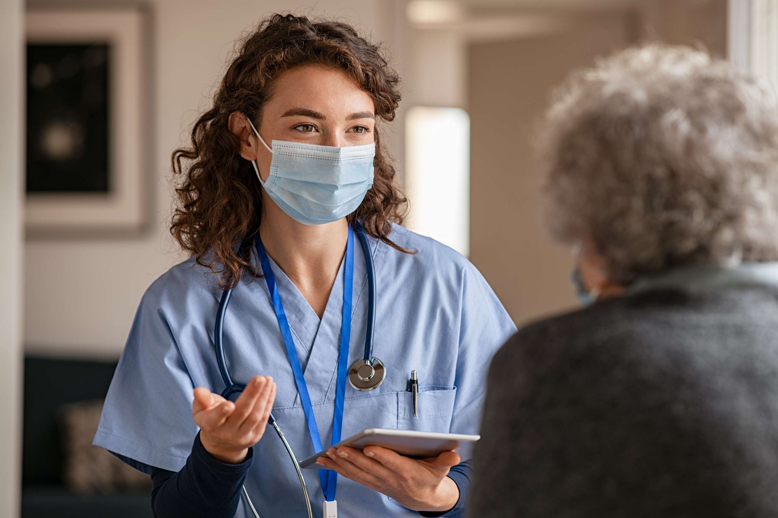 A nurse visits senior woman with surgical mask