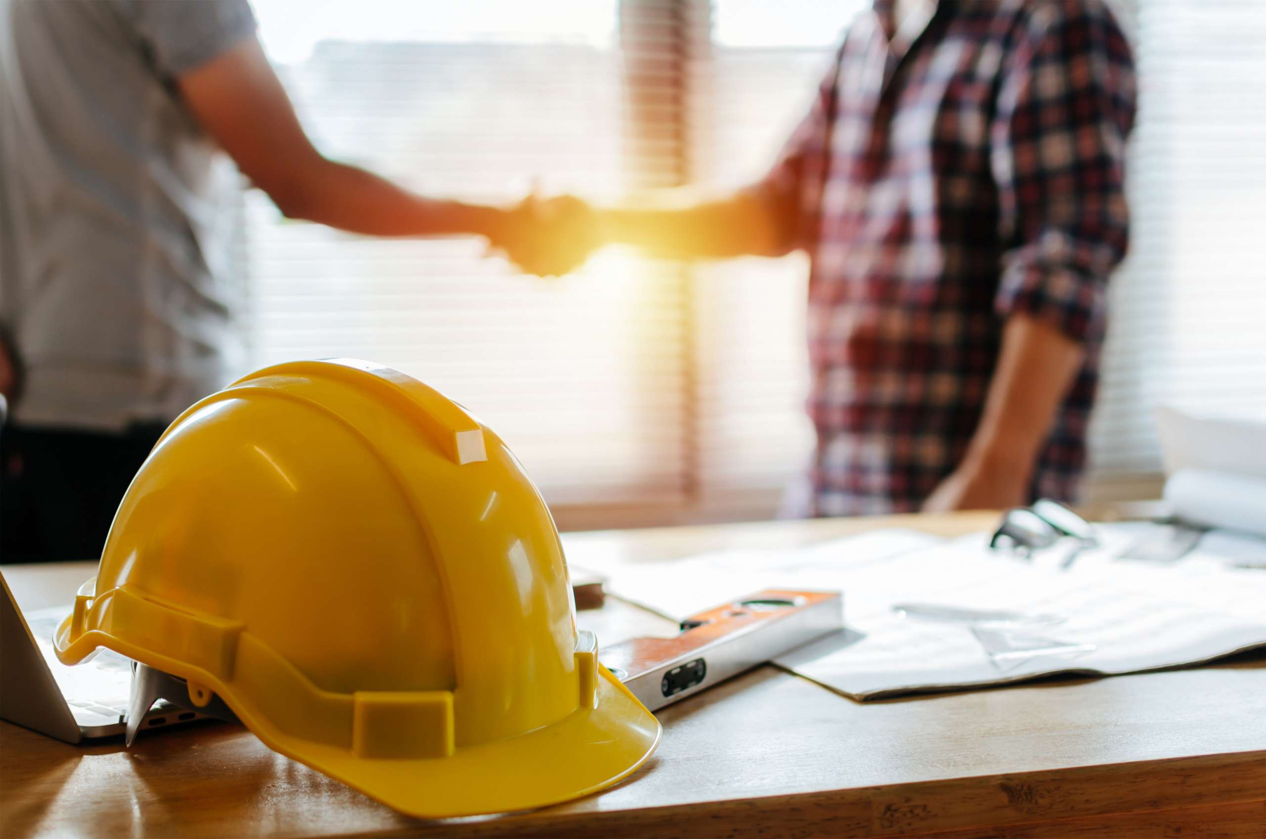 Consutruction contractor shakes hand in an office with yellow safety helmet to start up a business.