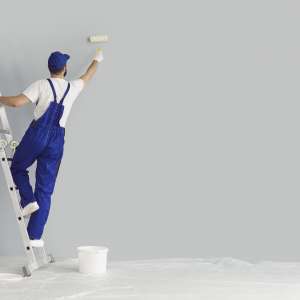 Painter paints grey wall with roller brush