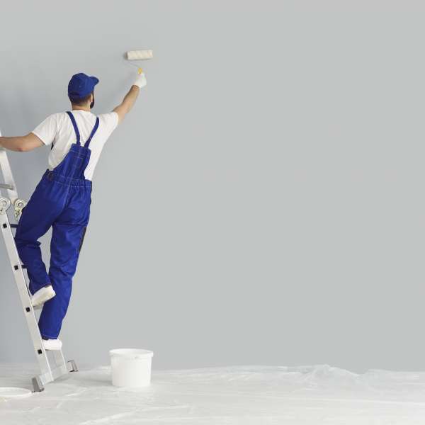 Painter paints grey wall with roller brush