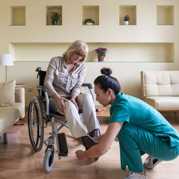 An elderly woman in a wheelchair is receiving a help from home health