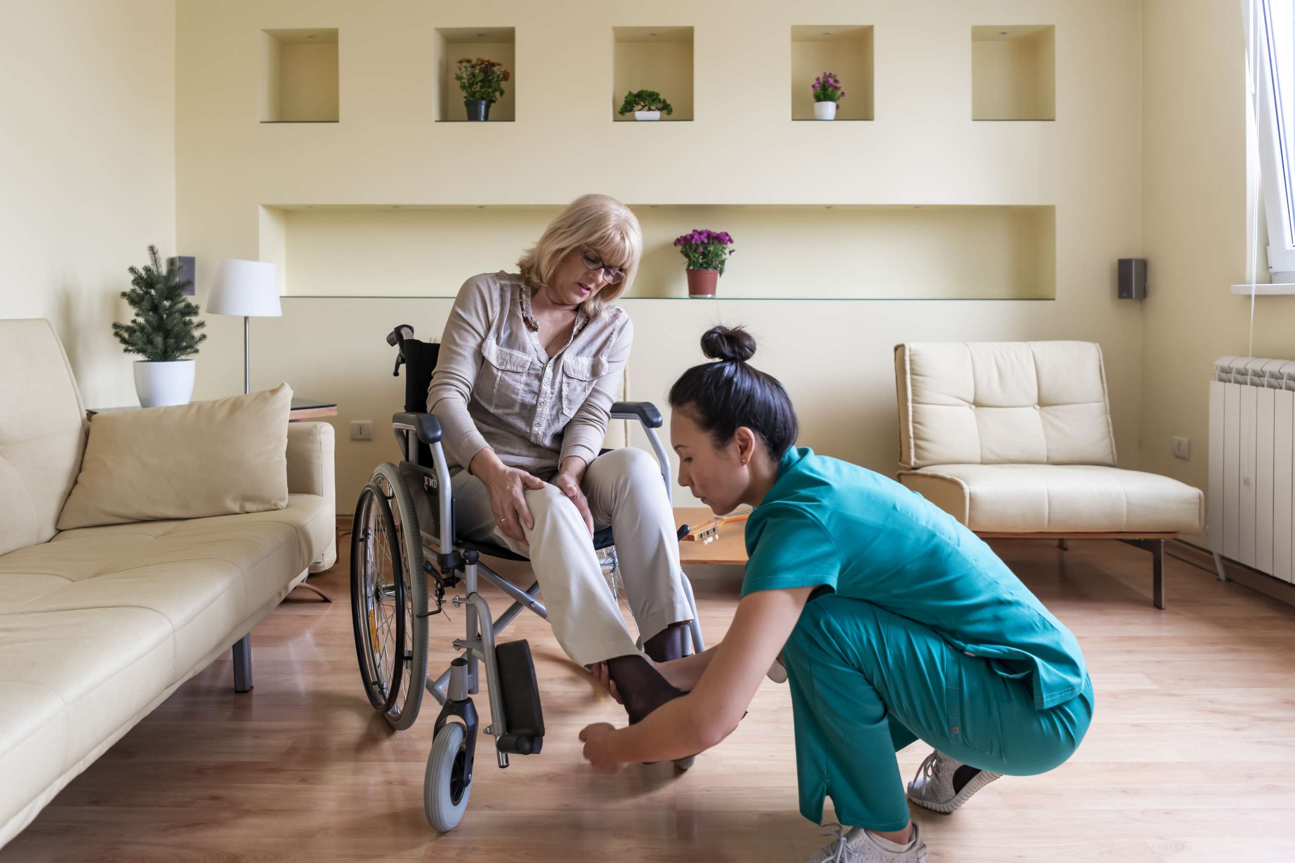 An elderly woman in a wheelchair is receiving a help from home health