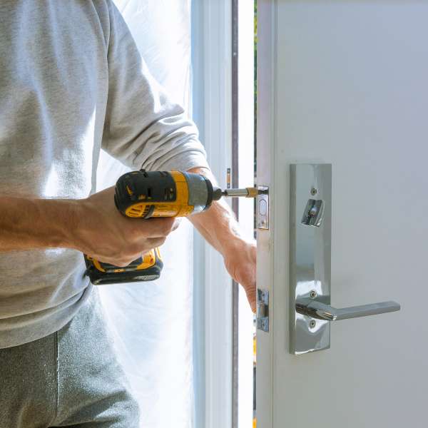 A handyman installs a lock in the door using a drill screwdriver