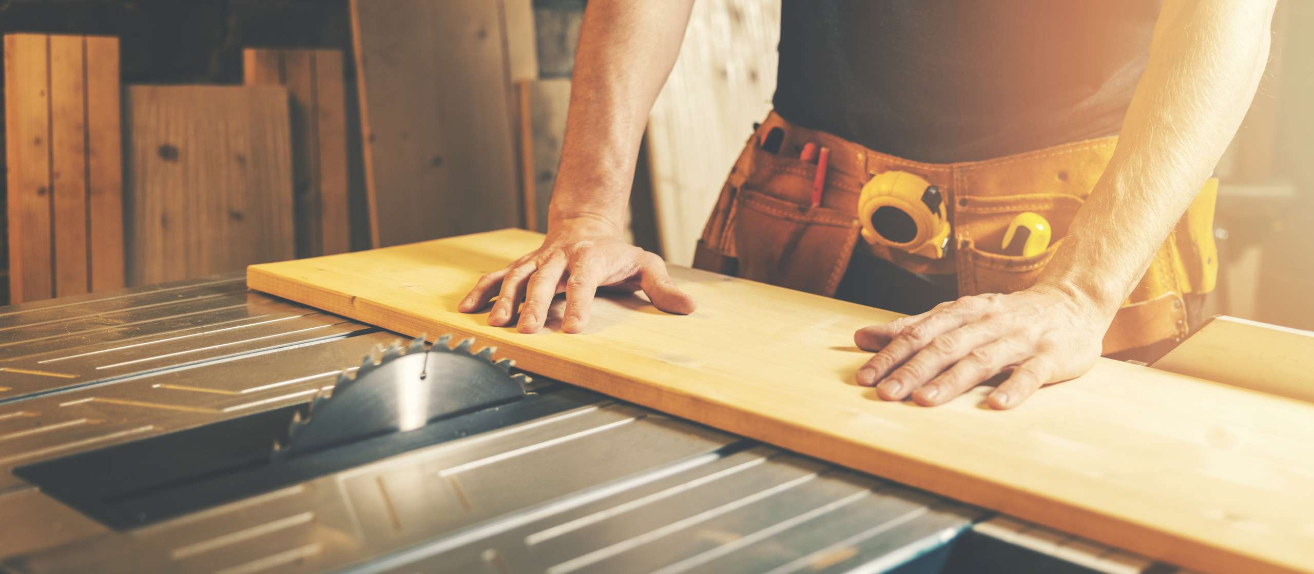 A carpenter cuts wooden board on a table saw.
