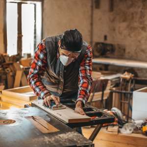 A carpenter cuts plank by circular saw in a workshop.