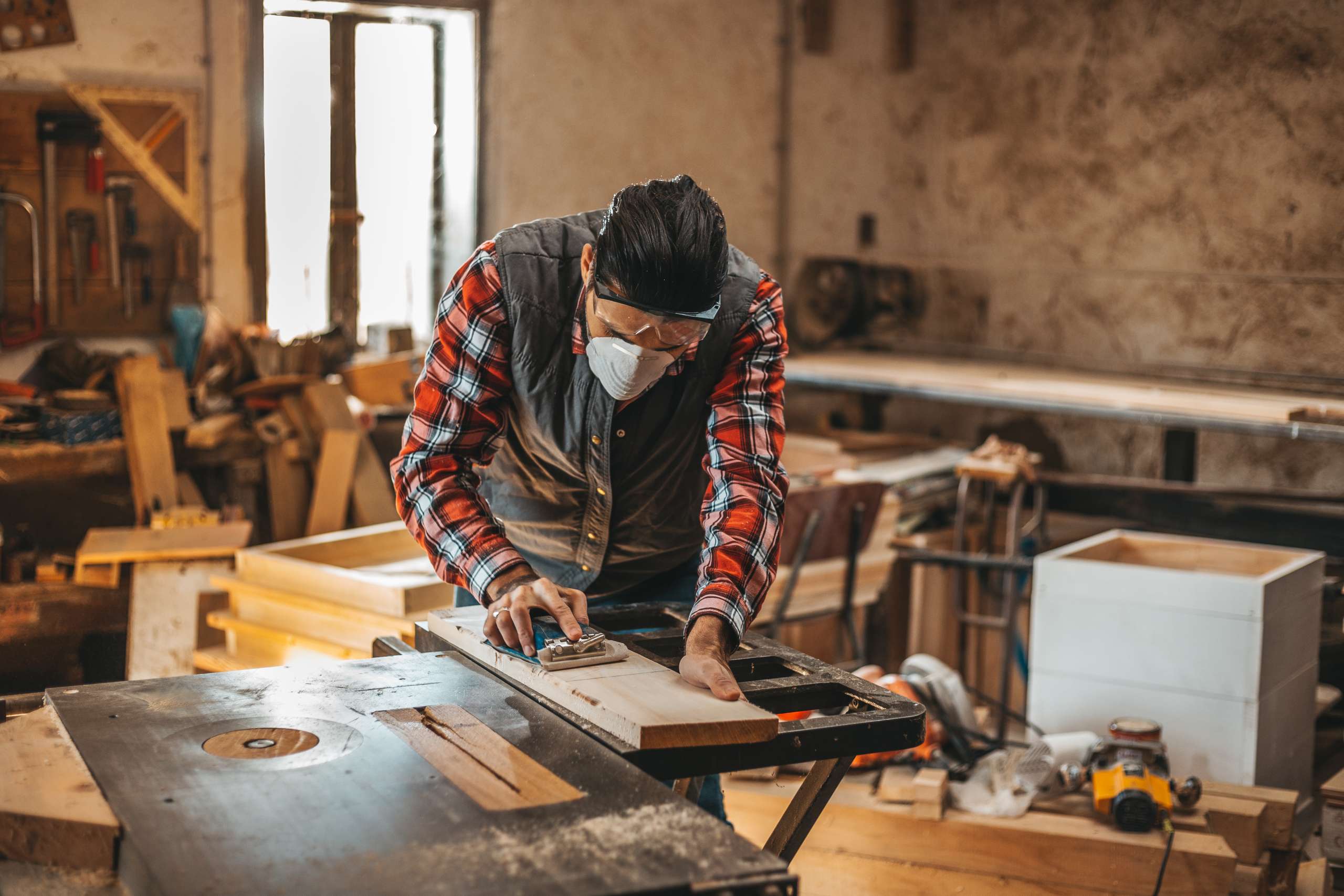 A carpenter cuts plank by circular saw in a workshop.