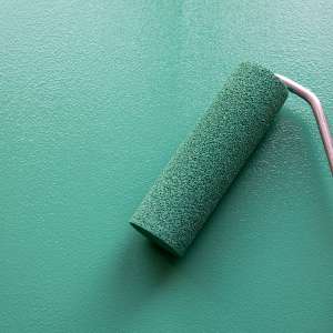 Paint roller with green colour on painted wooden surface.