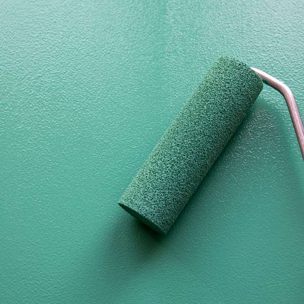 Paint roller with green colour on painted wooden surface.