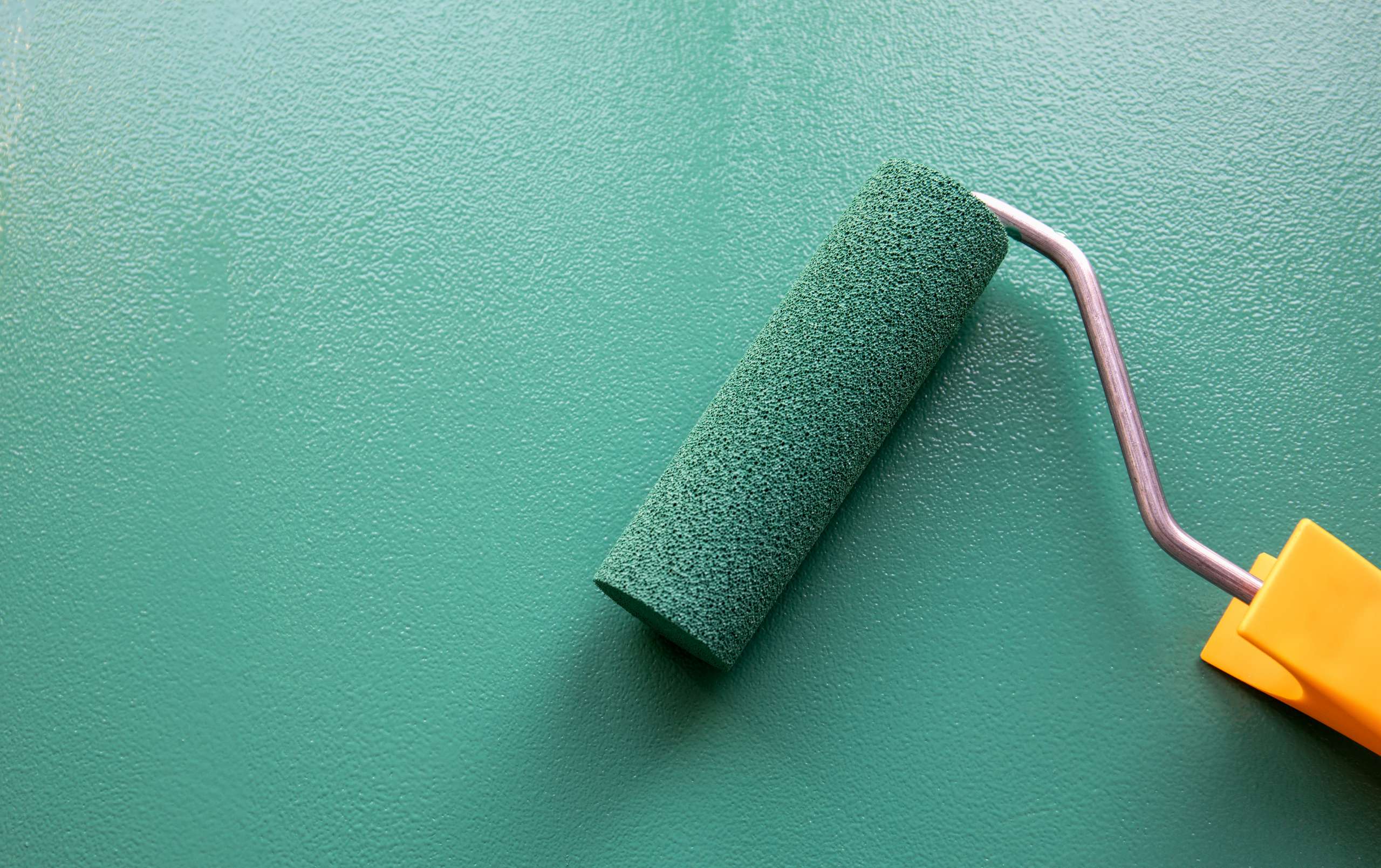 Paint roller with green colour on painted wooden surface.
