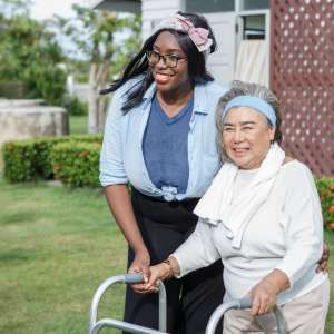 A senior woman with walker and carer in garden at home.