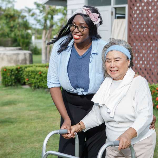 A senior woman with walker and carer in garden at home.