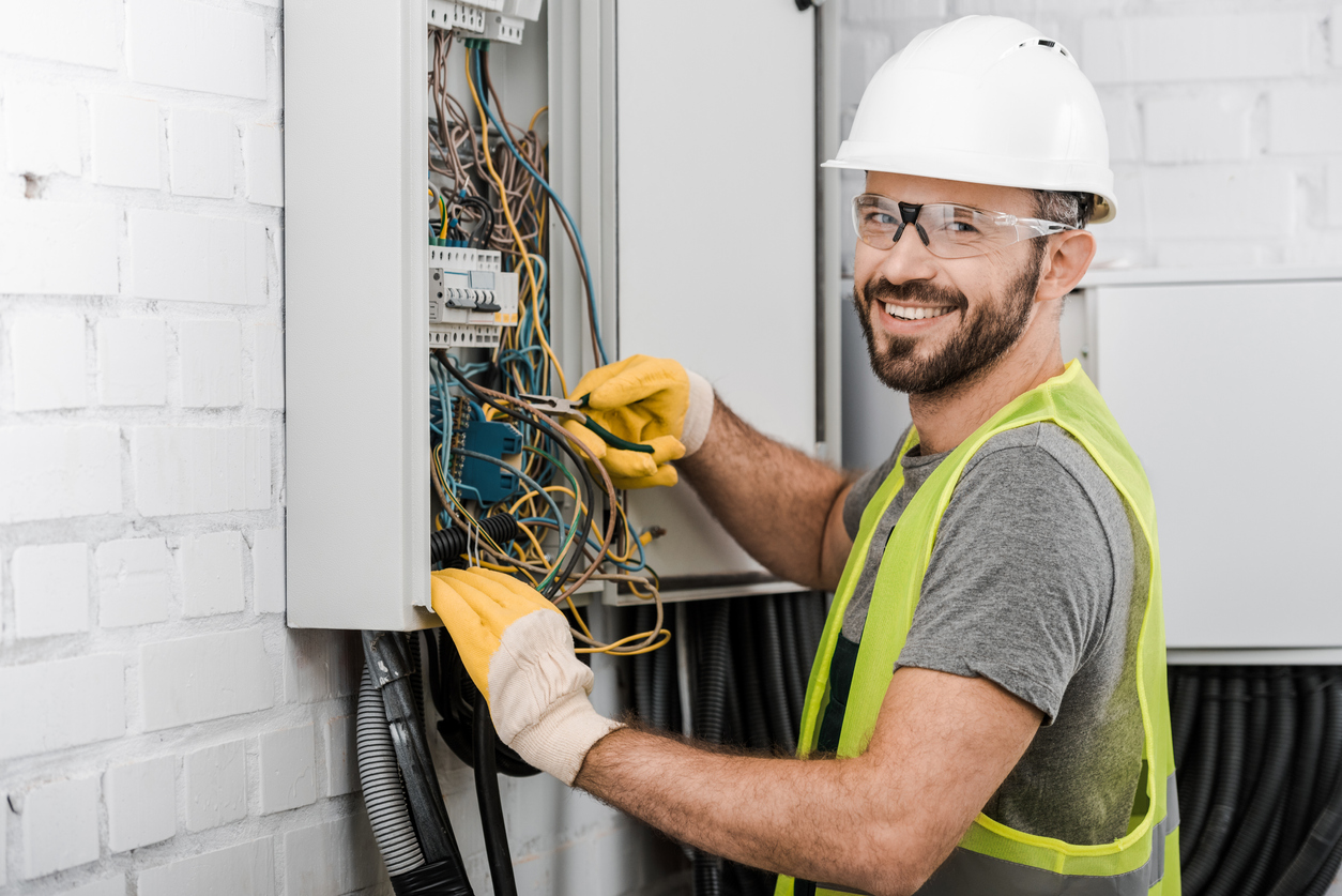 A smiling electrician repairing electrical box in corridor