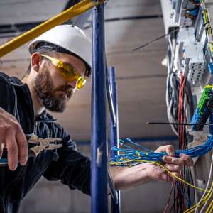 An electrician works in a switchboard with an electrical connecting cable.