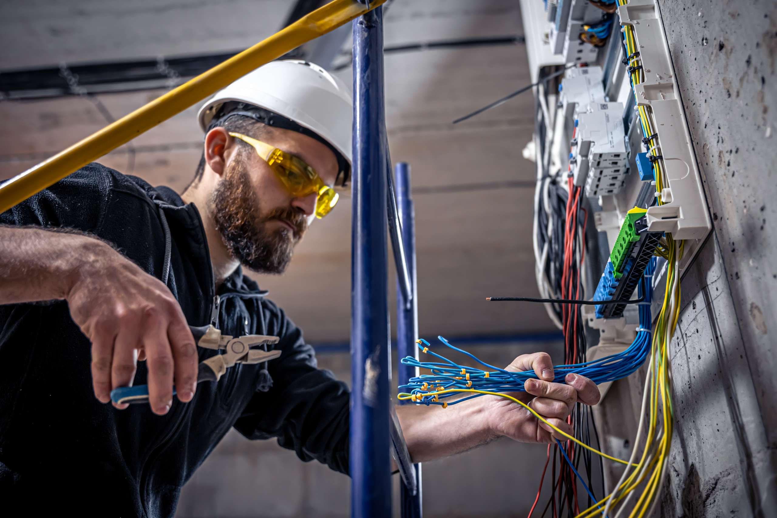 An electrician works in a switchboard with an electrical connecting cable.