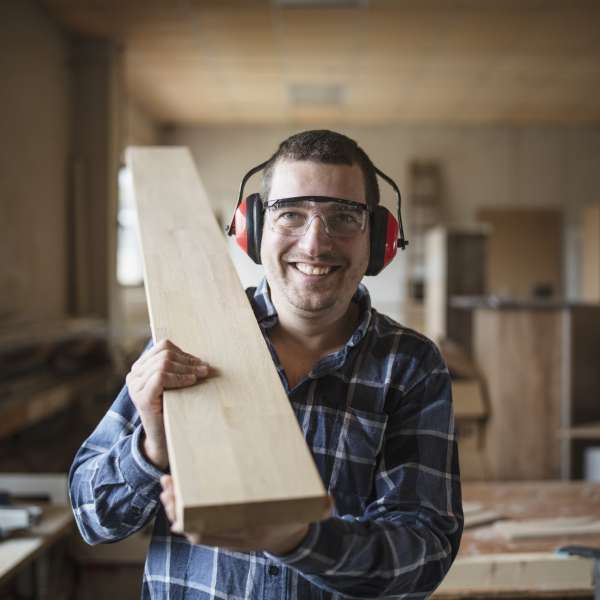 Smiling carpenter holding a wooden beam in workshop.