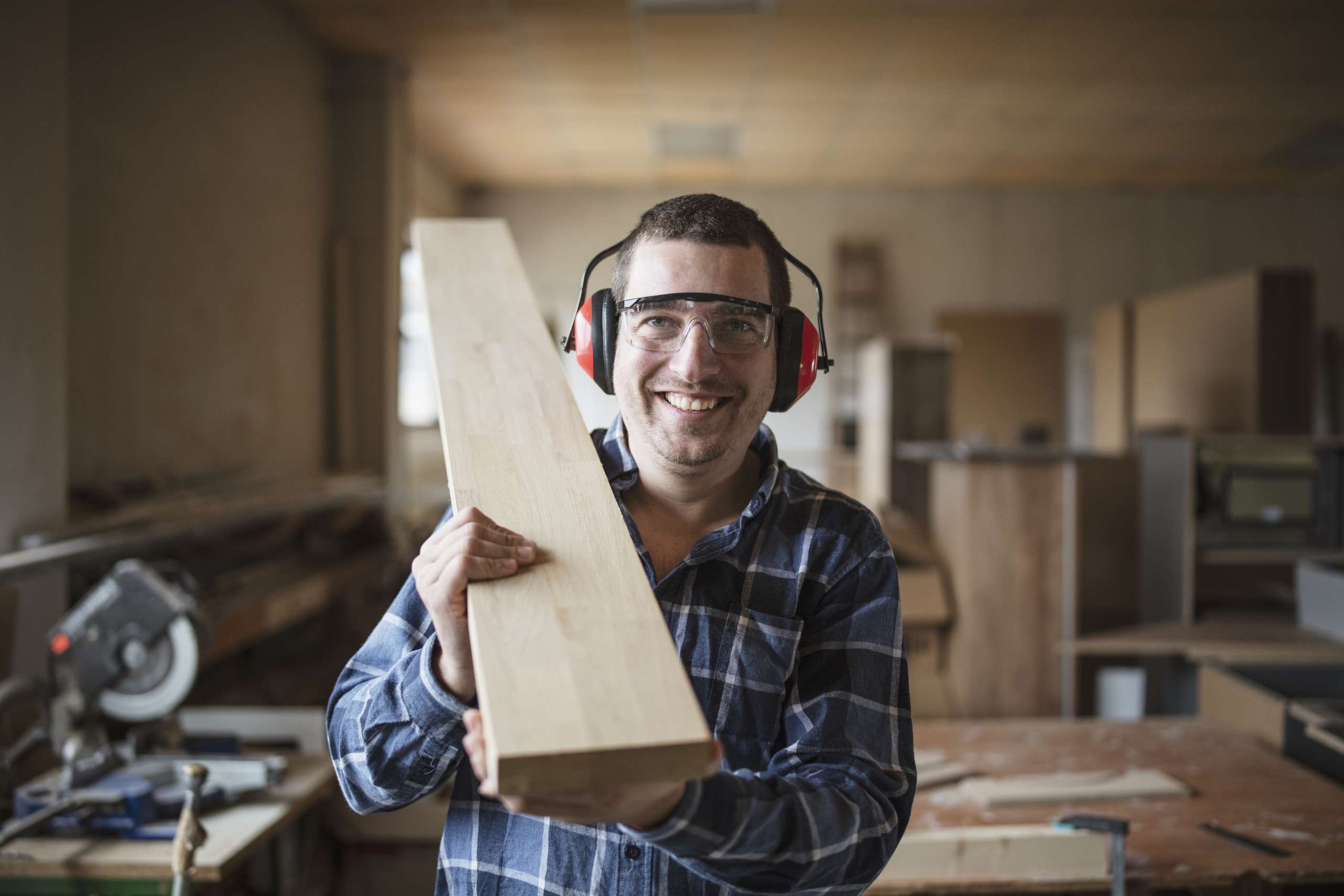 Smiling carpenter holding a wooden beam in workshop.