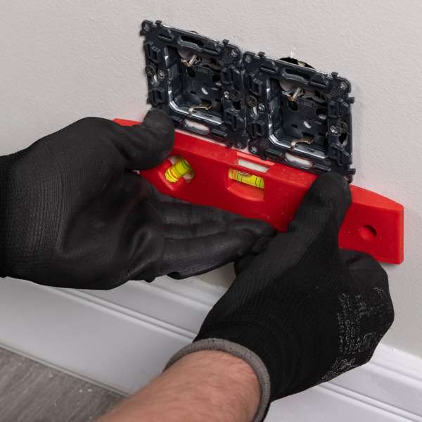 An electrician inserts a double grounded electrical outlet into the electrical box in the wall of the room.