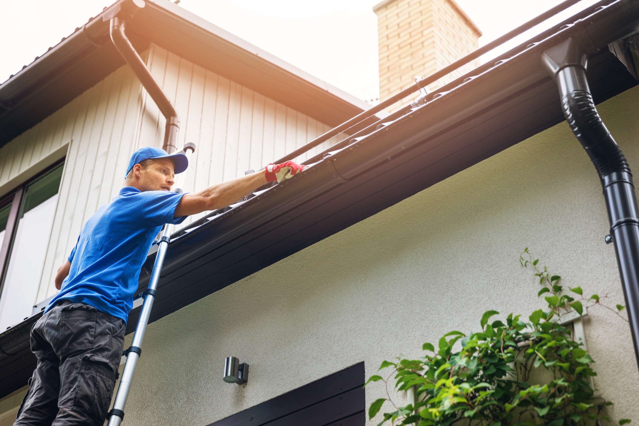 Handyman on ladder cleaning house gutter from leaves and dirt