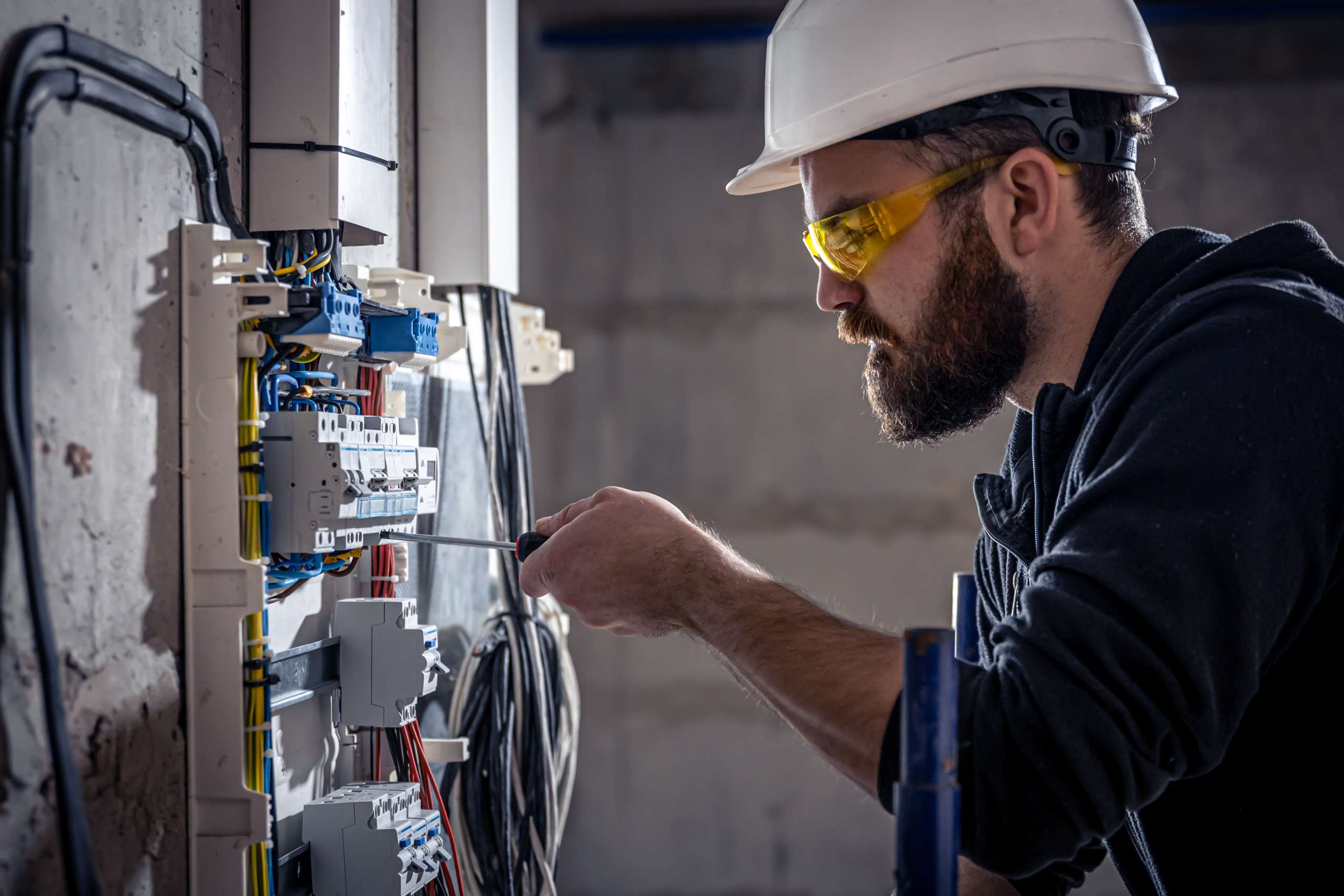 An electrician works in a switchboard with an electrical connecting cable.