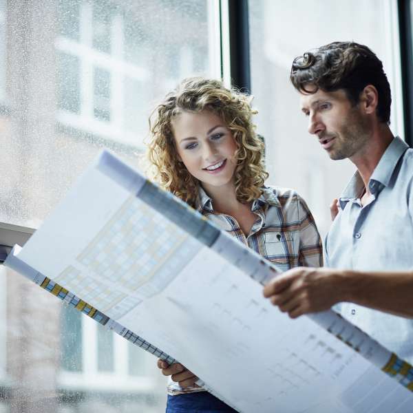 Two architects checking blueprint by window in modern studio