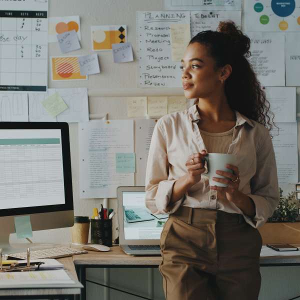 Shot of a young businesswoman standing and looking while holding a cup of coffee in her home office