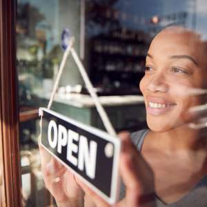 Owner Of Start Up Coffee Shop Or Restaurant Turning Round Open Sign On Door