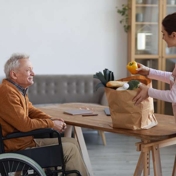 A female nurse assisting a senior man in wheelchair