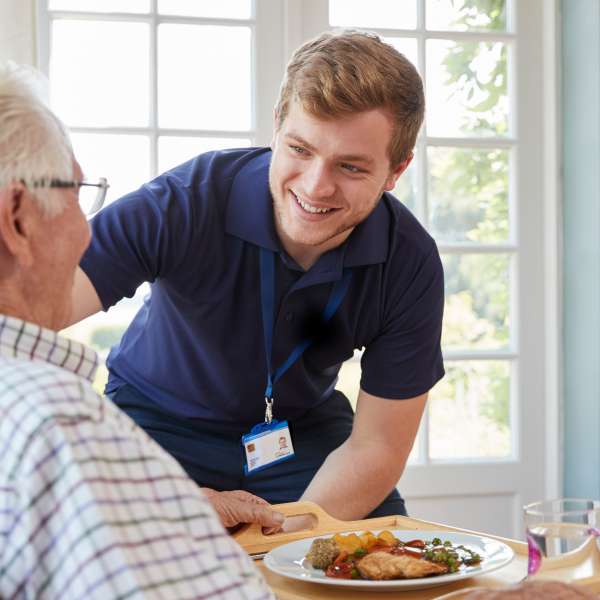 Male care worker serving dinner to a senior man at his home