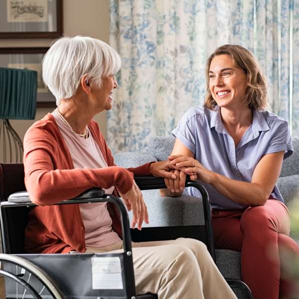 Mature woman comforting senior mom sitting on wheelchair at nursing home.