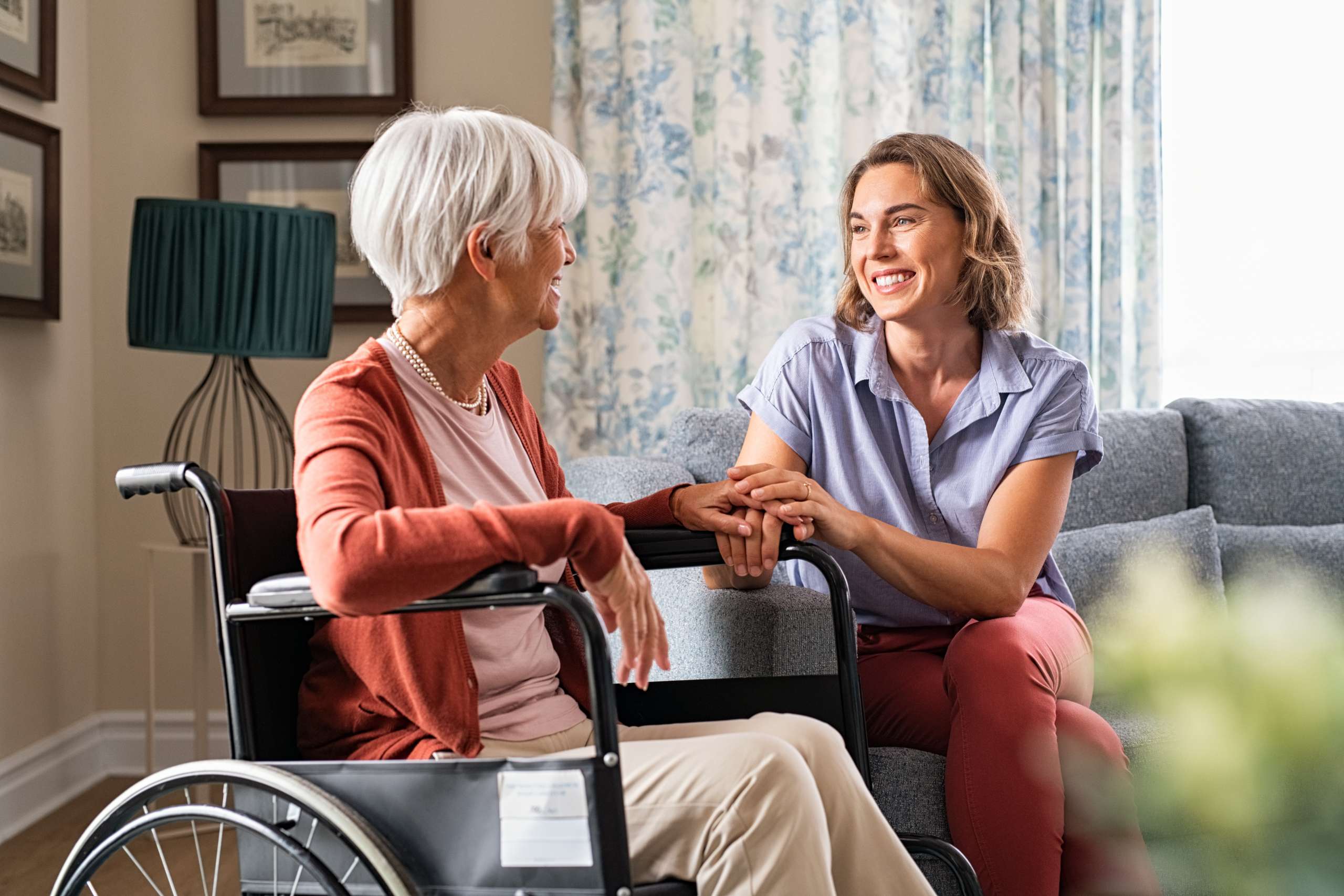 Mature woman comforting senior mom sitting on wheelchair at nursing home.