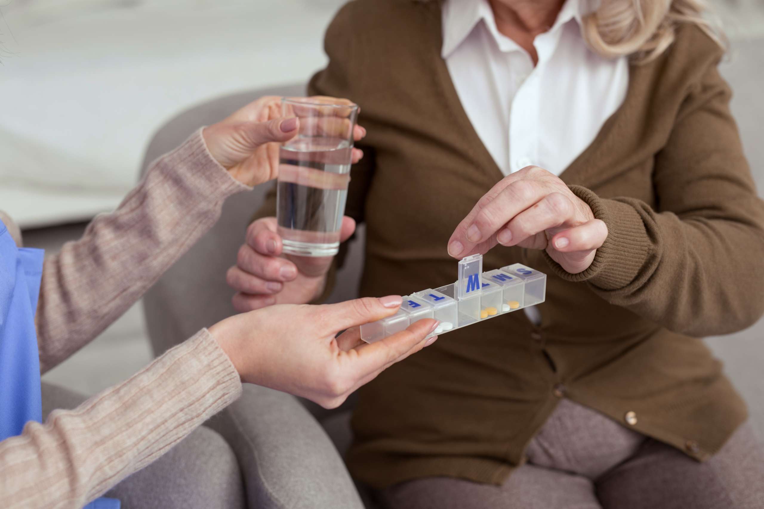 Female holding container for medication while giving glass with water to elder woman