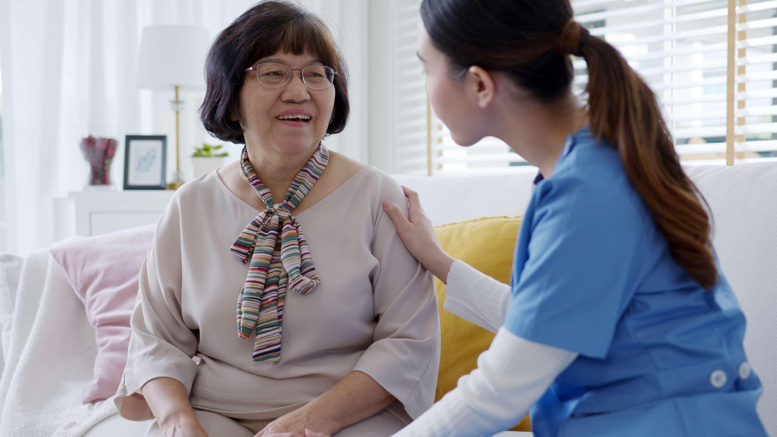 Young woman puts home care hand on senior grandmother shoulder to give support empathy in assisted living