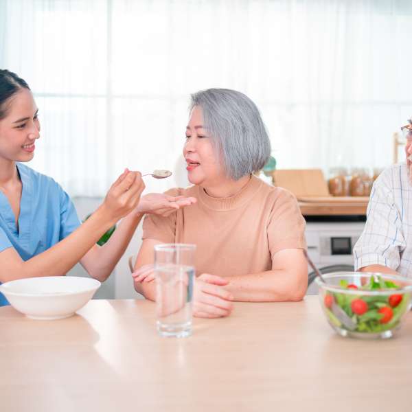 Homecare staff helps to serve a spoon of mush rice to senior woman.