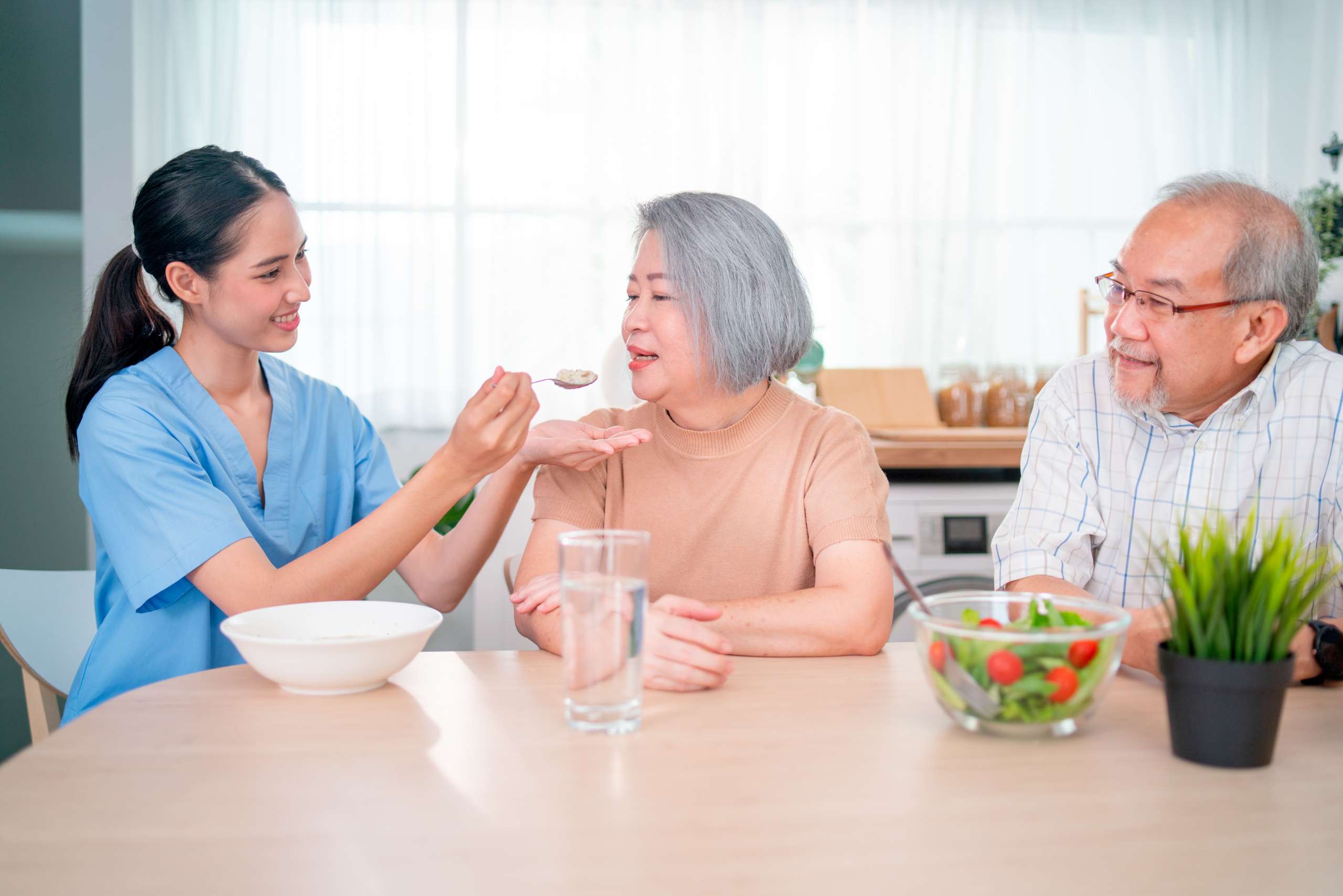 Homecare staff helps to serve a spoon of mush rice to senior woman.