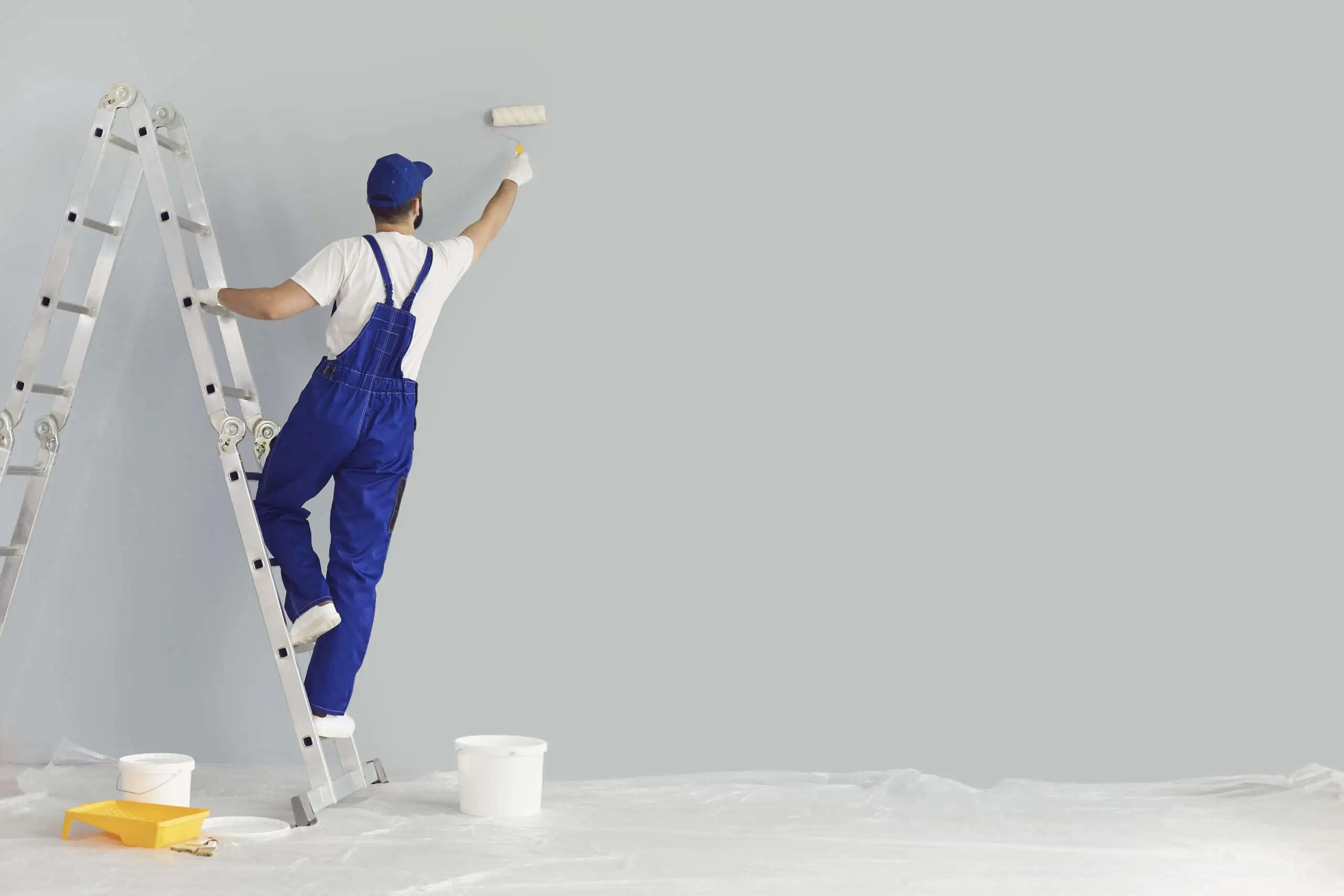 Painter paints grey wall with roller brush