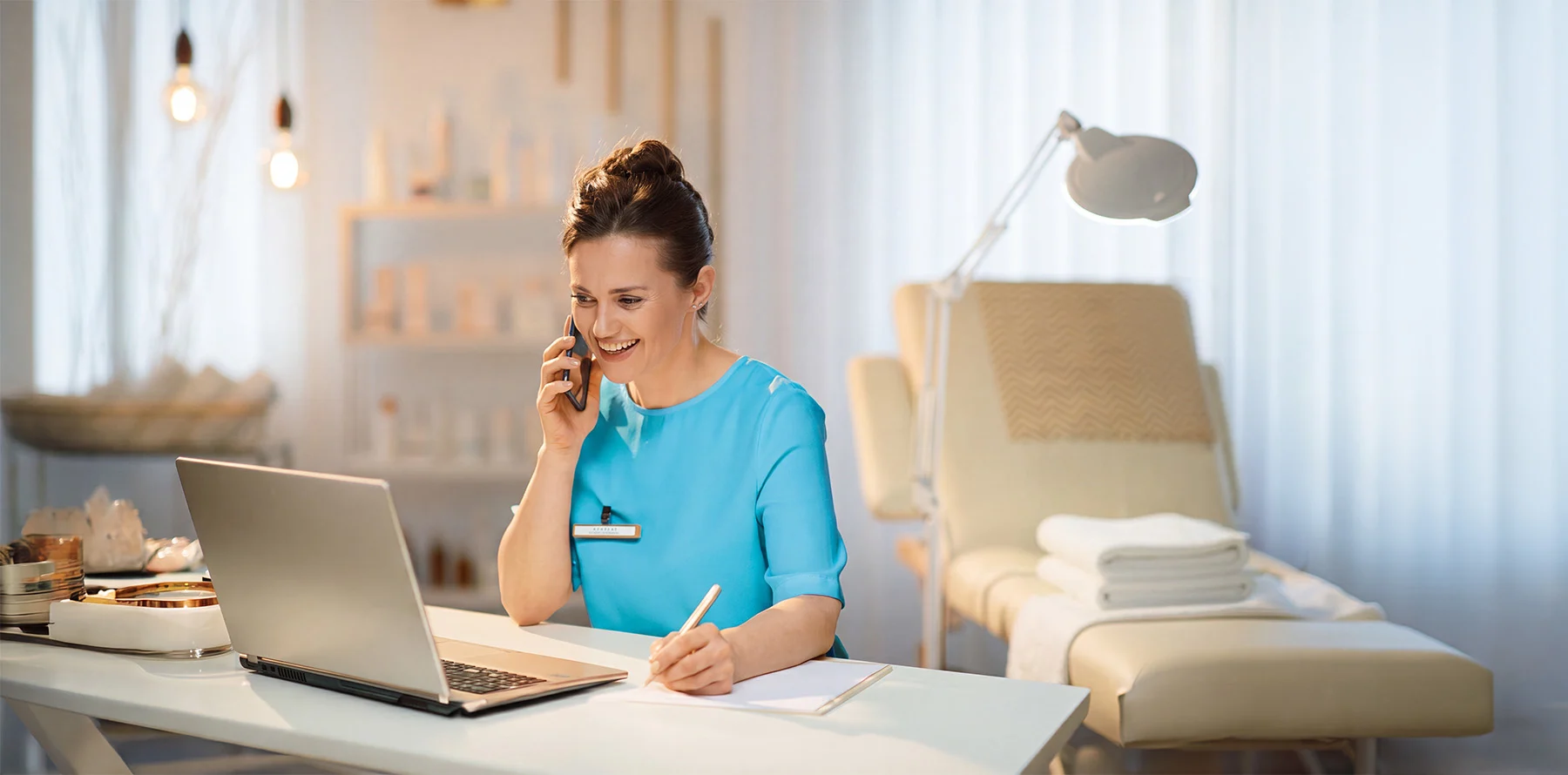Massage Therapist at workplace taking a call while working in front of her laptop